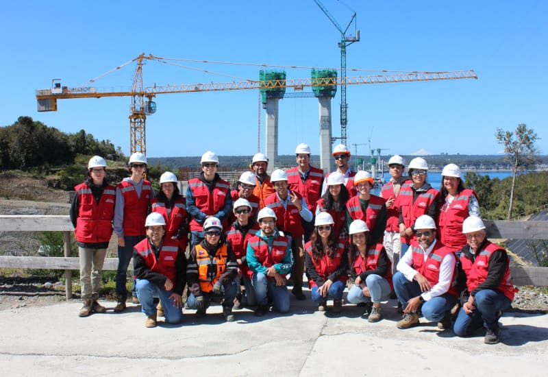 Grupo de estudiantes y profesores posando con puente en construción de fondo